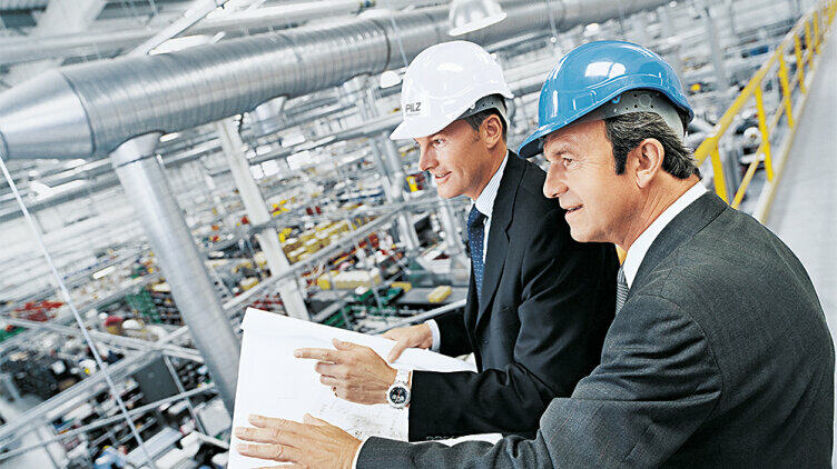 Two managers in safety helmets look down on a plant